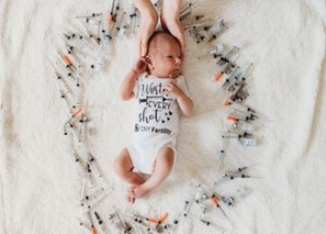 Image of infant surrounded by IVF injection needles, with two hands cradling the head